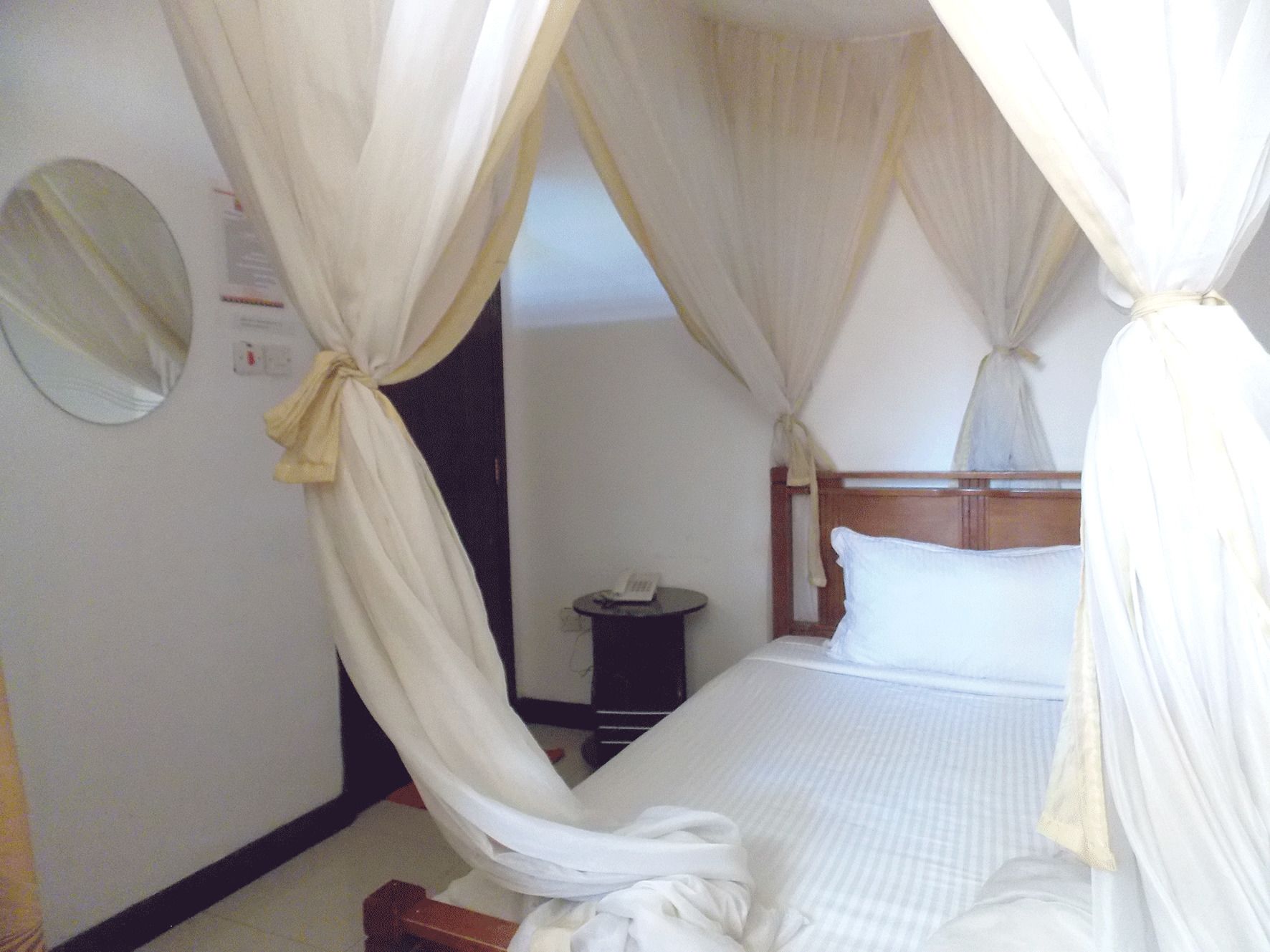 Una habitación de hotel con cama, mesita de noche, espejo y cortina.