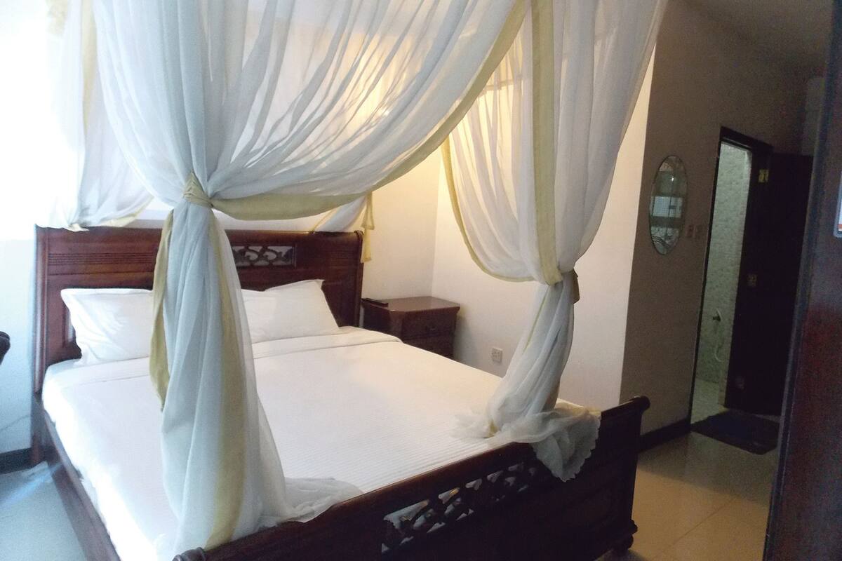 A bed with a canopy, a wooden headboard, and a nightstand with a lamp.