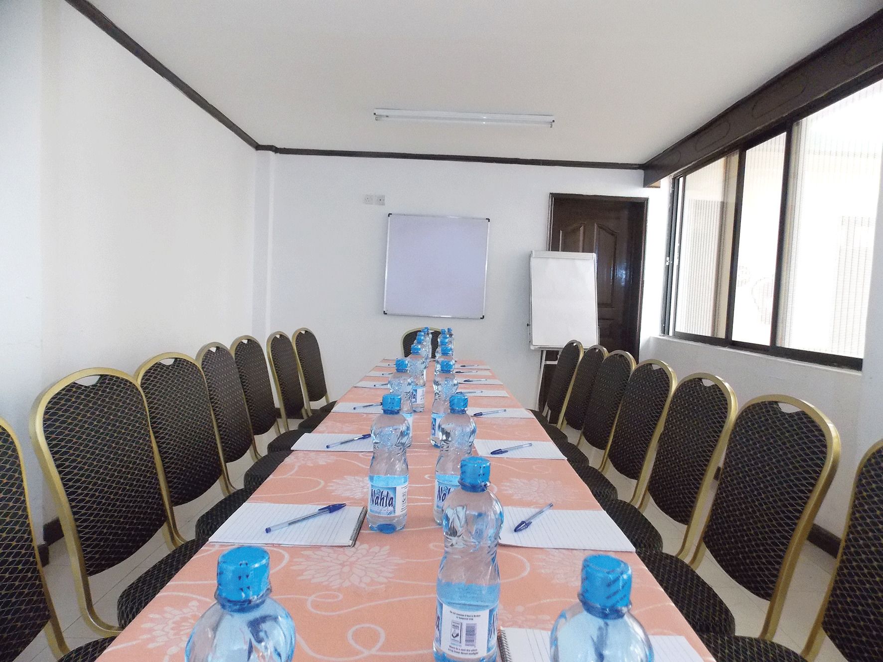 Un salón de conferencias con una larga mesa, sillas, botellas de agua y una pizarra.