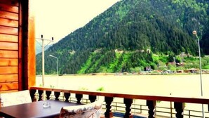 A wooden cabin with a balcony overlooking a river and a forested mountain. - Doğa Motel (Çaykara)