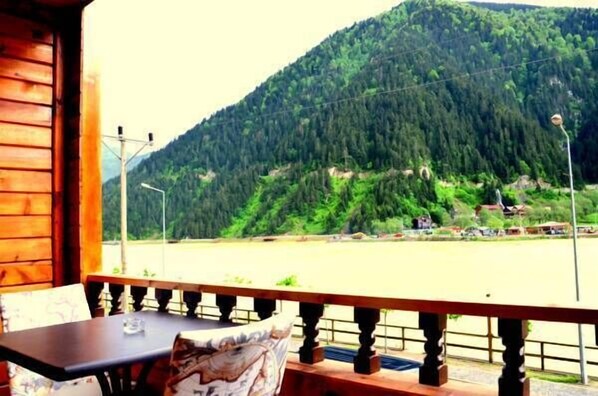A wooden cabin with a balcony overlooking a river and a forested mountain.