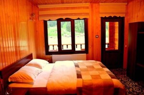 A wooden room with a bed, a window with a view of greenery, and a door. - Doğa Motel (Çaykara)