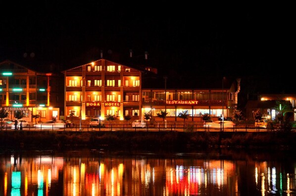 A hotel with multiple floors, a visible restaurant, and a reflection in the water.