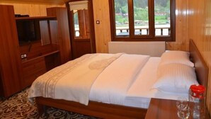 A wooden room with a bed, a small table, and a window with a view of greenery. - Doğa Motel (Çaykara)