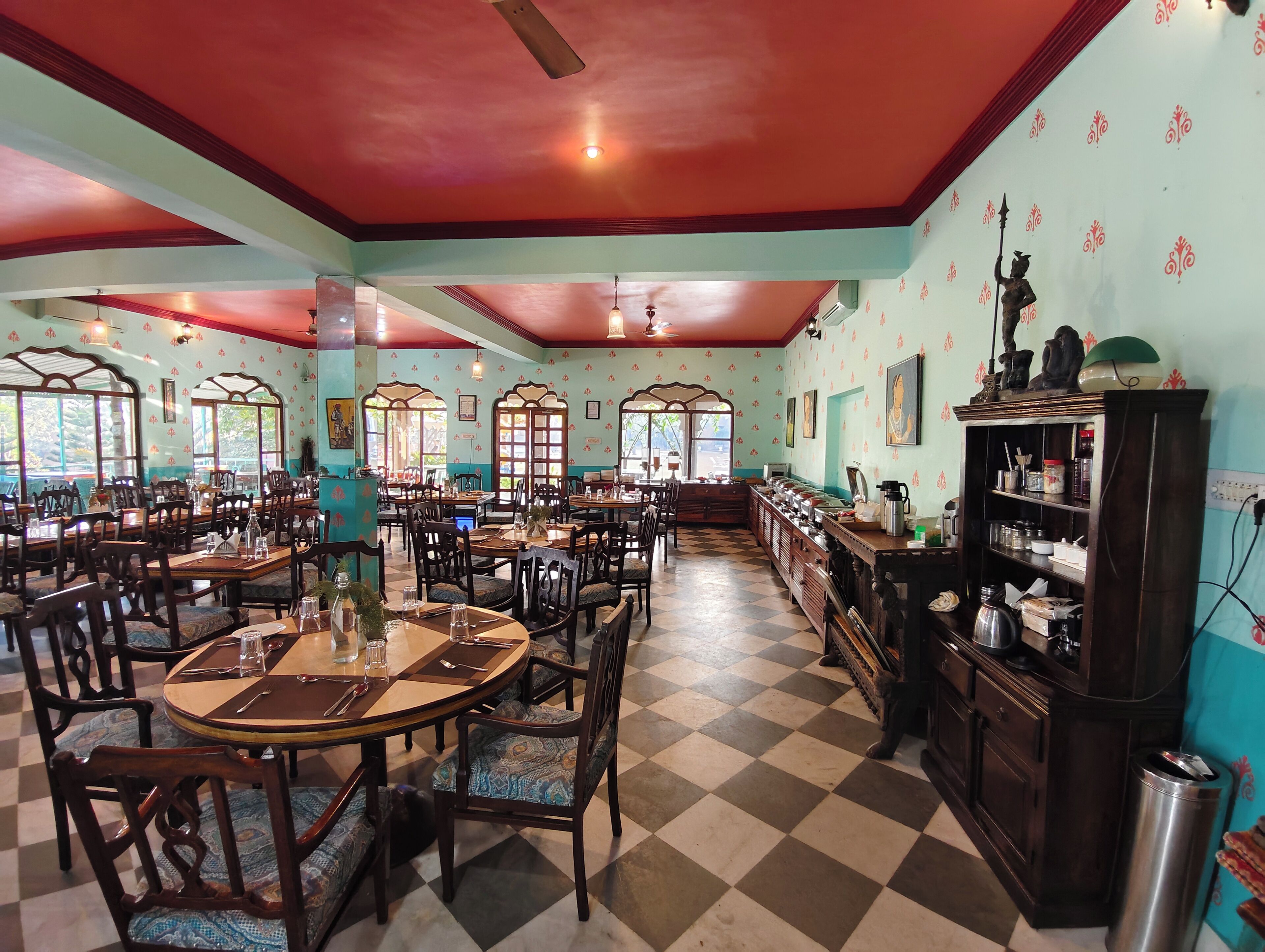A restaurant with multiple dining tables and chairs, a checkered floor, and decorative wall patterns.