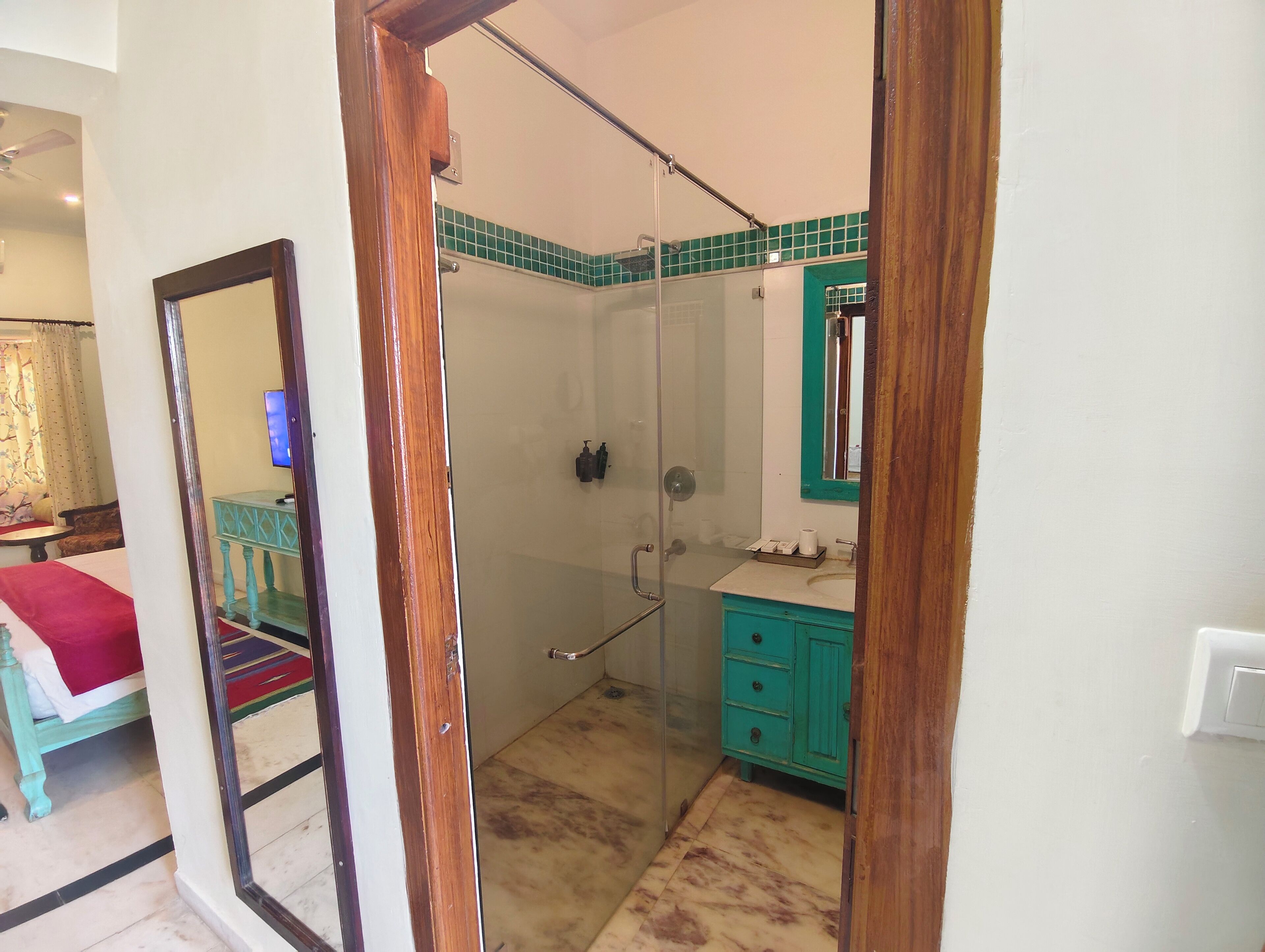 Un baño con cabina de ducha de vidrio, lavabo con gabinete verde y espejo con marco de madera.