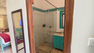 Un baño con cabina de ducha de vidrio, lavabo con gabinete verde y espejo con marco de madera.