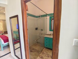 Un bagno con box doccia in vetro, lavabo con mobiletto verde e specchio con cornice in legno.
