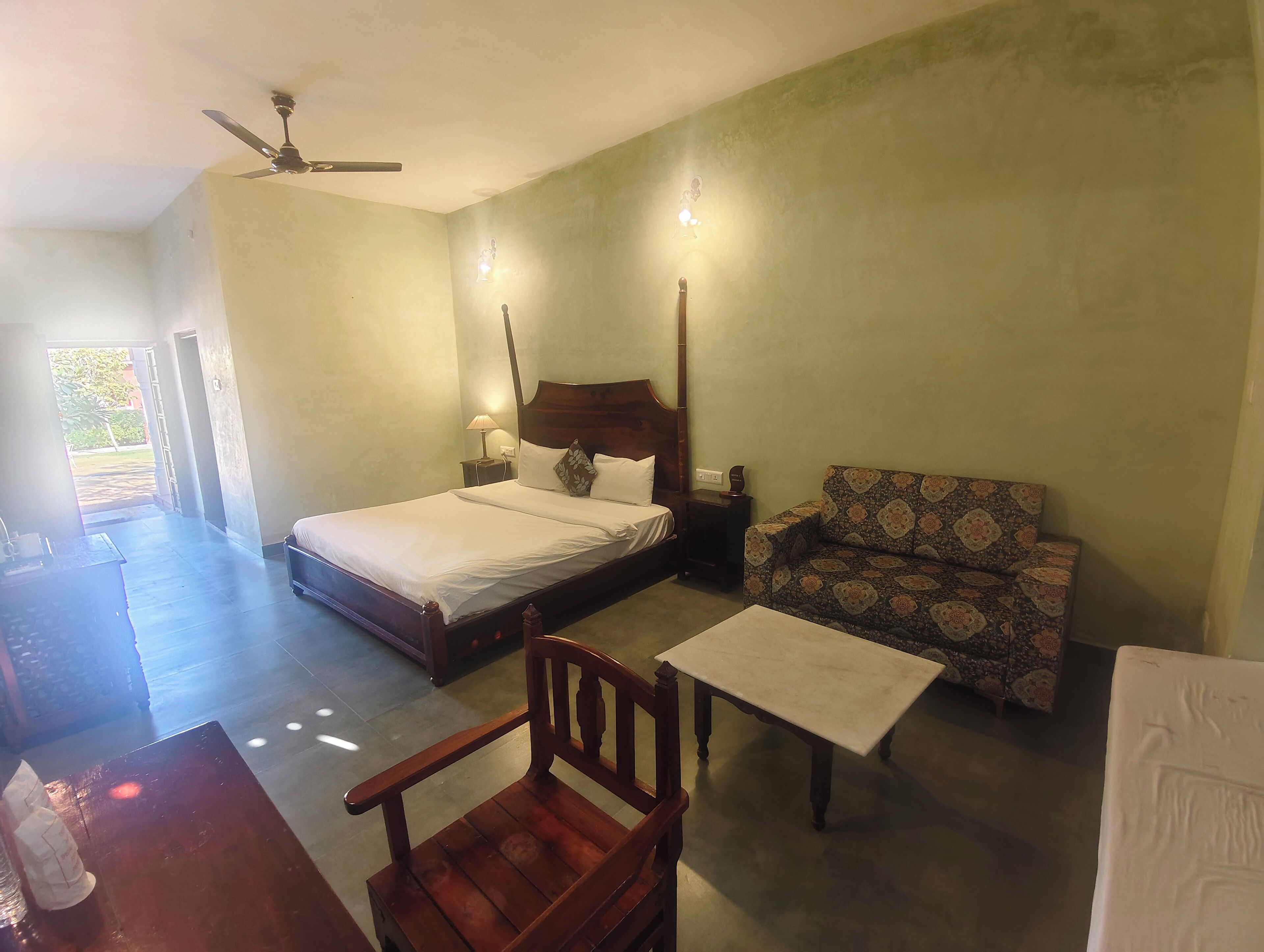 A bedroom with a bed, a wooden chair, a sofa, a small table, and a ceiling fan.
