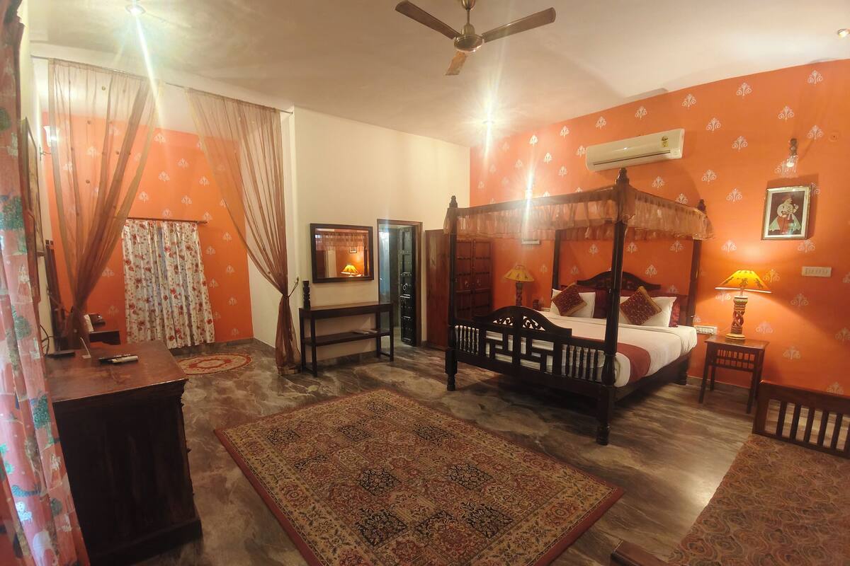 A room with a four-poster bed, a wooden desk, a small table, and a chair.