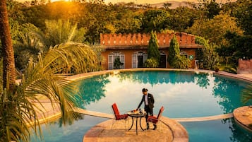 Una piscina con una zona de estar circular y un edificio al fondo.