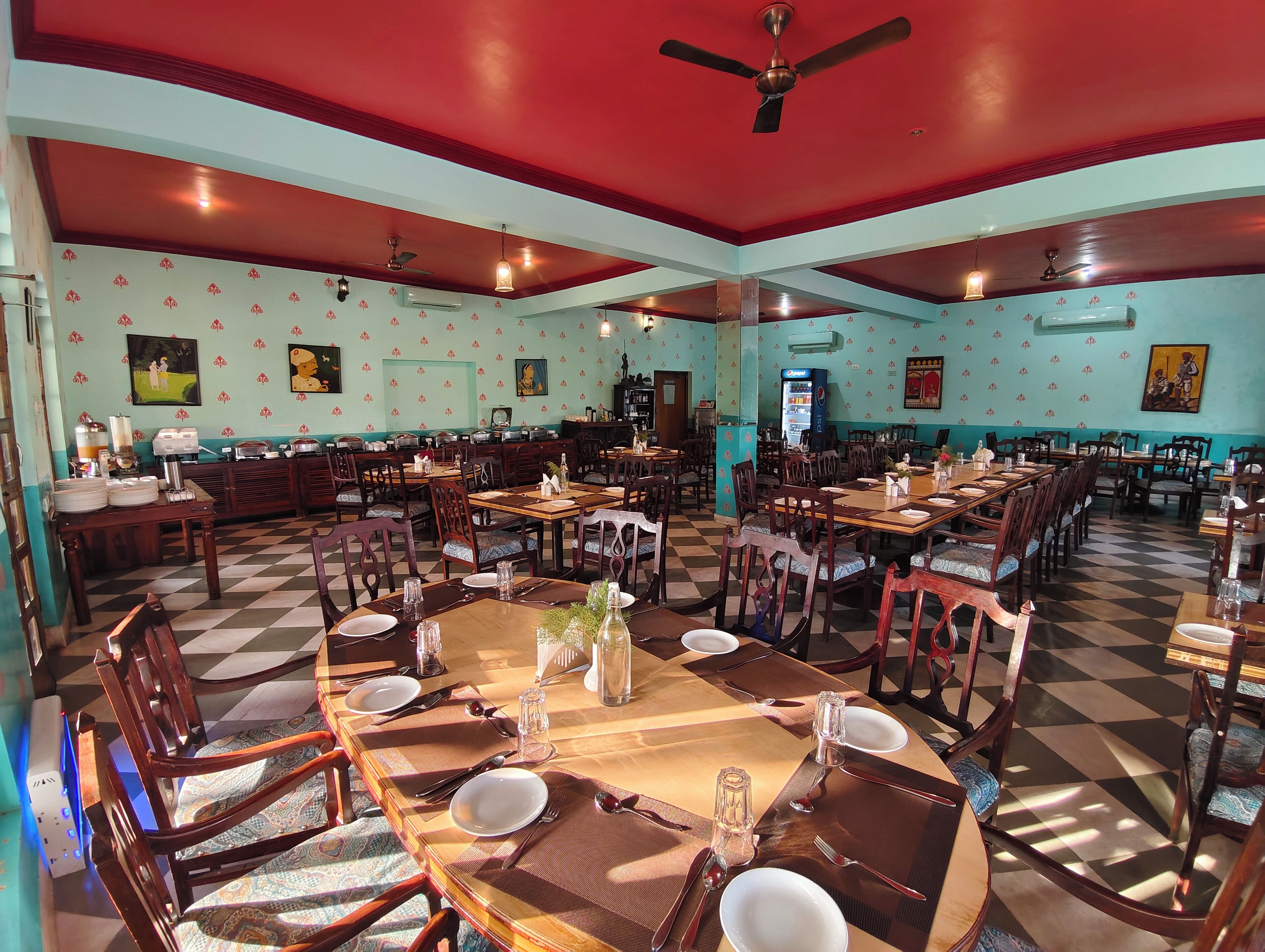 Una sala ristorante con diversi tavoli e sedie, condizionatori d'aria e ventilatori a soffitto.