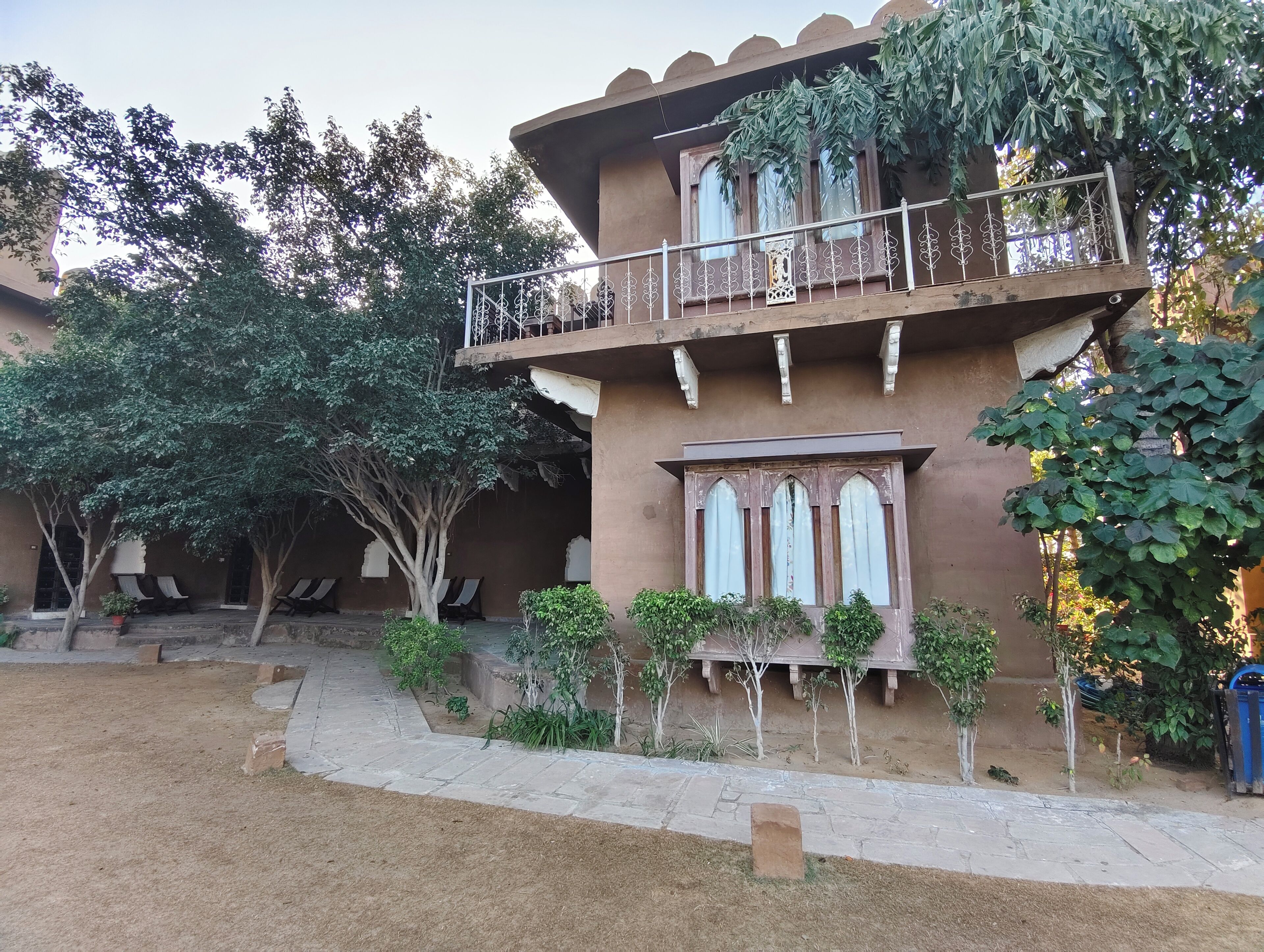 Un bâtiment à deux étages doté d’un balcon, entouré d’arbres et de plantes en pot.
