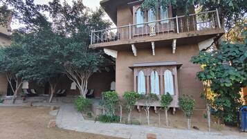 A two-story building with a balcony, surrounded by trees and potted plants.