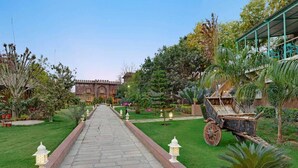 A pathway leading to a building with a traditional architectural style, surrounded by well-maintained gardens and a decorative cart.