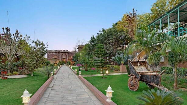 A pathway leading to a building with a traditional architectural style, surrounded by well-maintained gardens and a decorative cart. - Pushkar Fort - Luxury Heritage Resort  (Pushkar)