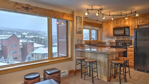 A kitchen with a large island, wooden cabinets, and a view of a snowy landscape. - Sky Mountain Studio (Breckenridge)
