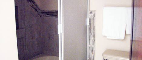 A bathroom with a glass shower enclosure, a toilet, and a towel hanging on the wall.