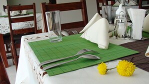 Ein Esstisch, gedeckt mit einer grünen Tischunterlage, weißen Servietten, Besteck, einem Glas und einer gelben Blume.