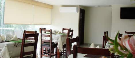 A dining area with tables set for four, wooden chairs, and a window with blinds.