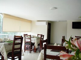 Comedor con mesas dispuestas para cuatro, sillas de madera y un ventanal con persianas.
