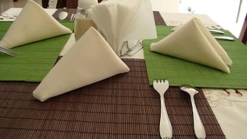 Una mesa con servilletas blancas dobladas en forma de triángulo, un tenedor y una cuchara sobre un mantel de bambú.