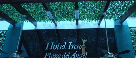 A sign for Hotel Inn Plaza del Angel with a modern design and a ceiling fan.
