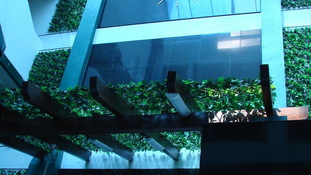 Ein modernes Hotelinnere mit einem zentralen Atrium, begrünten Pflanzenwänden und einem Deckenventilator.