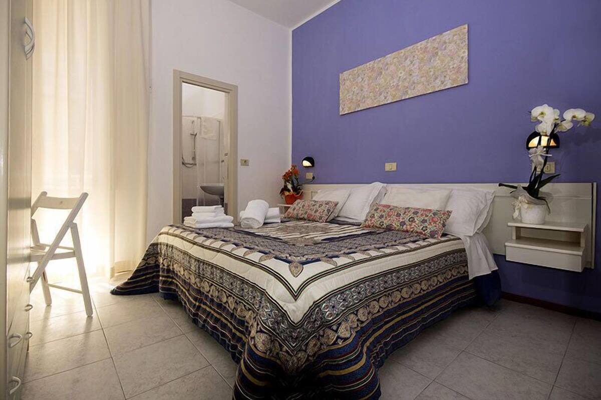 A bedroom with a large bed, a chair, a nightstand, and a wall-mounted shelf.