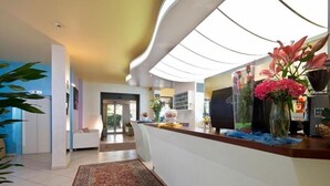 A reception area with a curved ceiling, a reception desk, a large rug, and a plant. - Hotel Milano (Gatteo)
