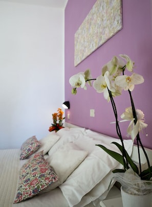 A bedroom with a bed, pillows, a vase with orchids, and a wall art piece. - Hotel Milano (Gatteo)