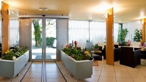 A spacious lobby with a modern design, featuring a central glass door entrance, comfortable seating areas, and potted plants. - Hotel Milano (Gatteo)