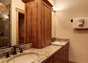 A bathroom with a wooden vanity, a granite countertop, a sink, and a mirror.