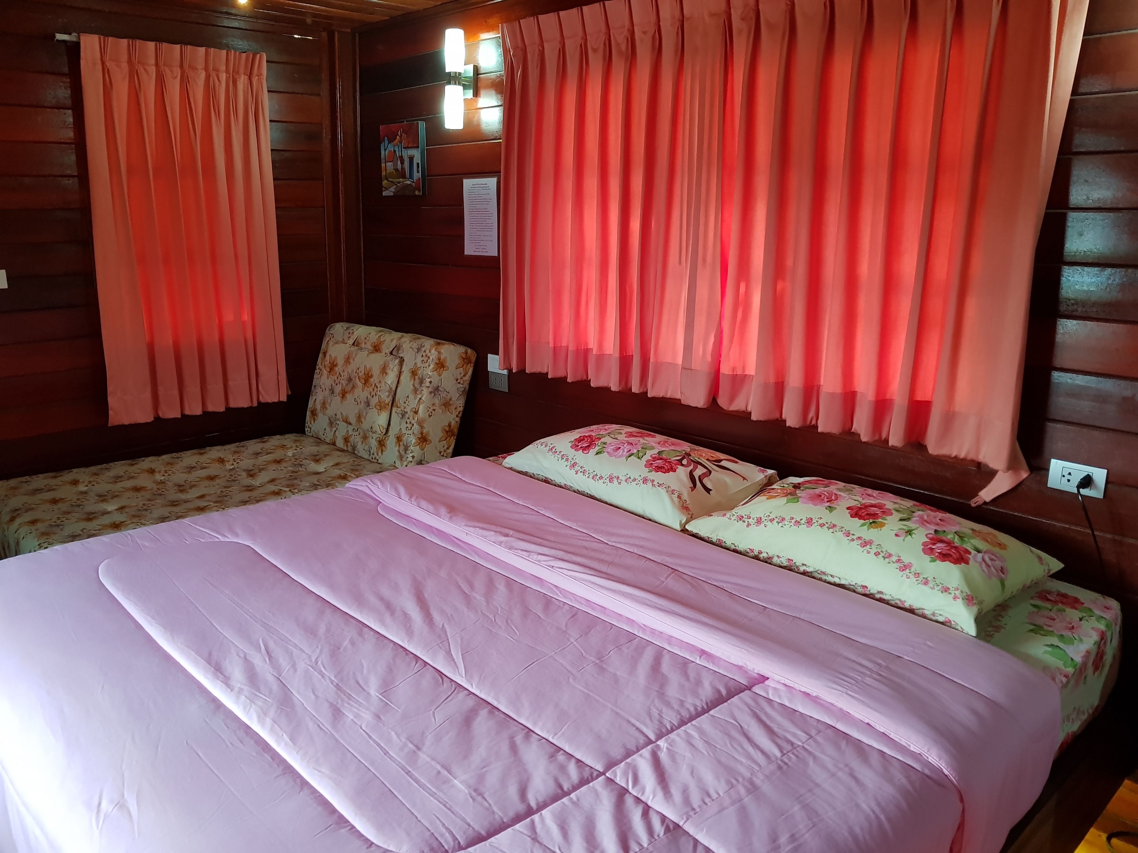 A room with a large bed, two smaller beds, floral-patterned headboards, and red curtains.