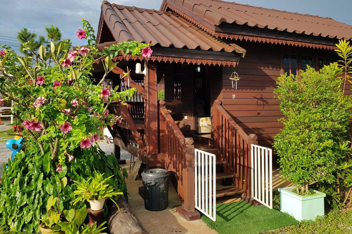A wooden house with a porch, a small garden, and a trash bin.