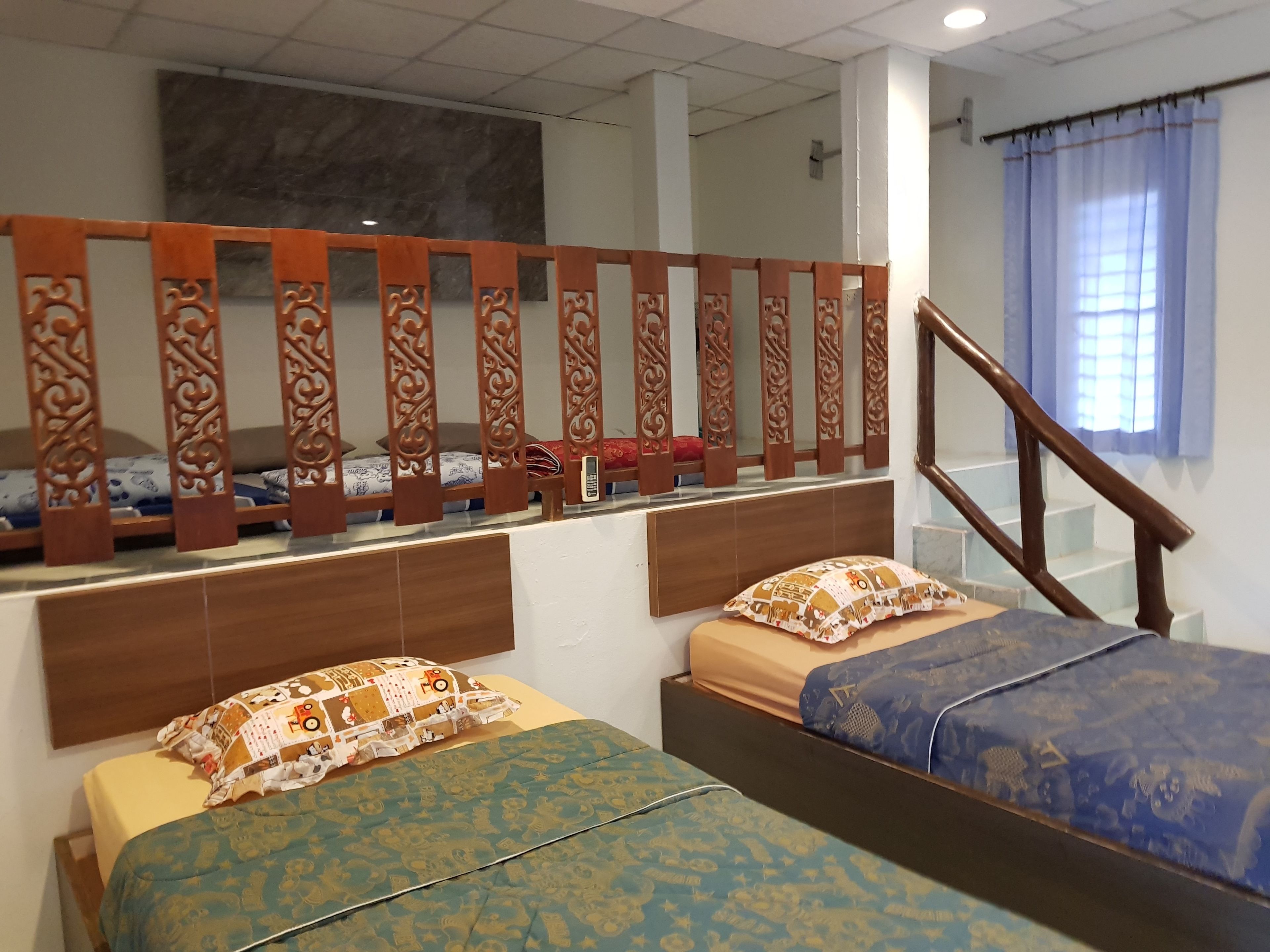 Camera d'albergo con due letti, una testiera in legno, un pannello decorativo, una scala e una finestra con tende.