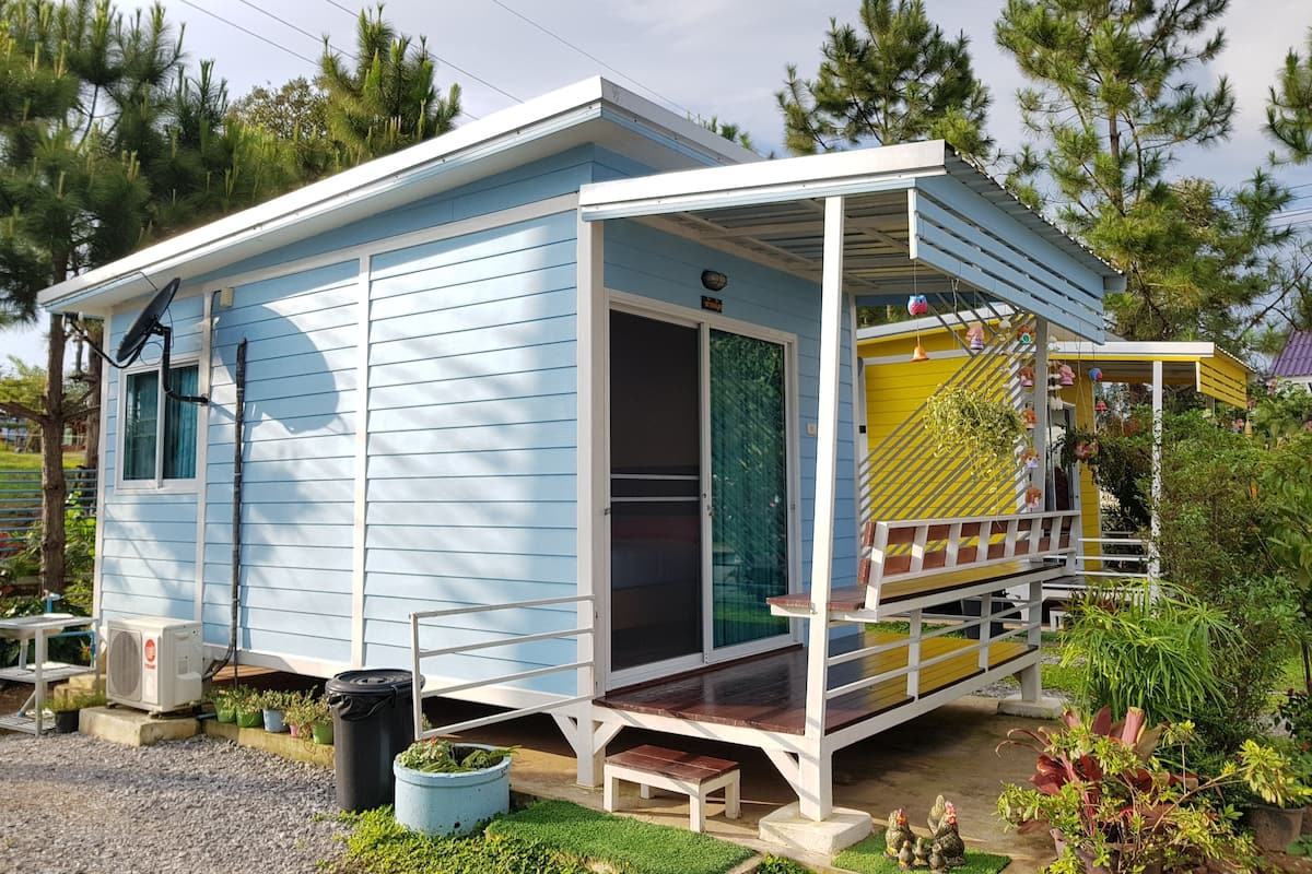 A small, single-story house with a porch, a satellite dish, and a small garden area.
