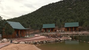 A lakeside lodge with a sandy beach, a small dock, and a forested hill in the background. - Holmstead Ranch Resort (Veyo)