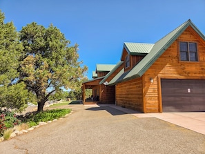 A wooden cabin with a covered porch, a garage, and a driveway leading to the entrance. - Holmstead Ranch Resort (Veyo)