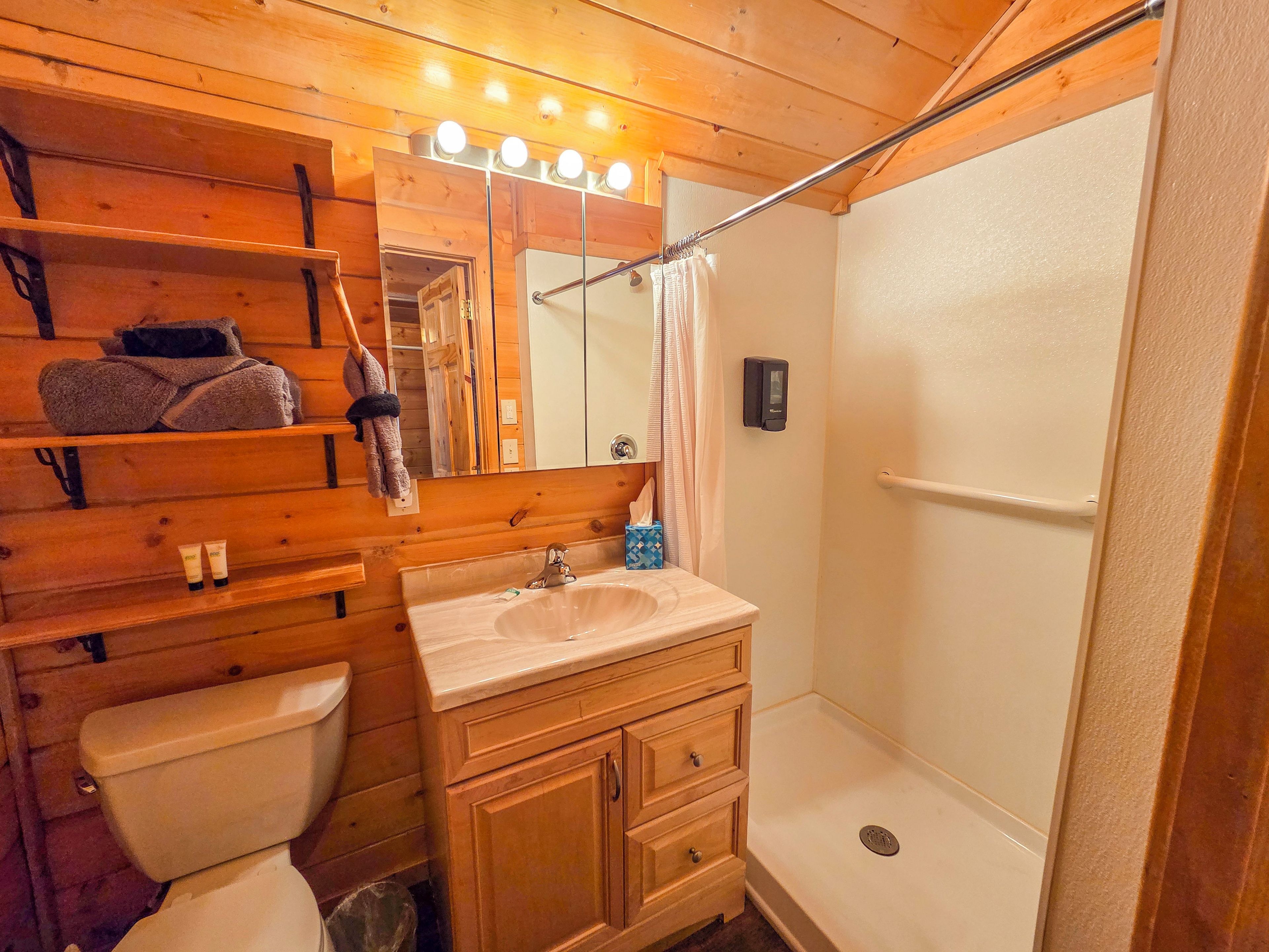 Un baño de madera con lavamanos, espejo y ducha.