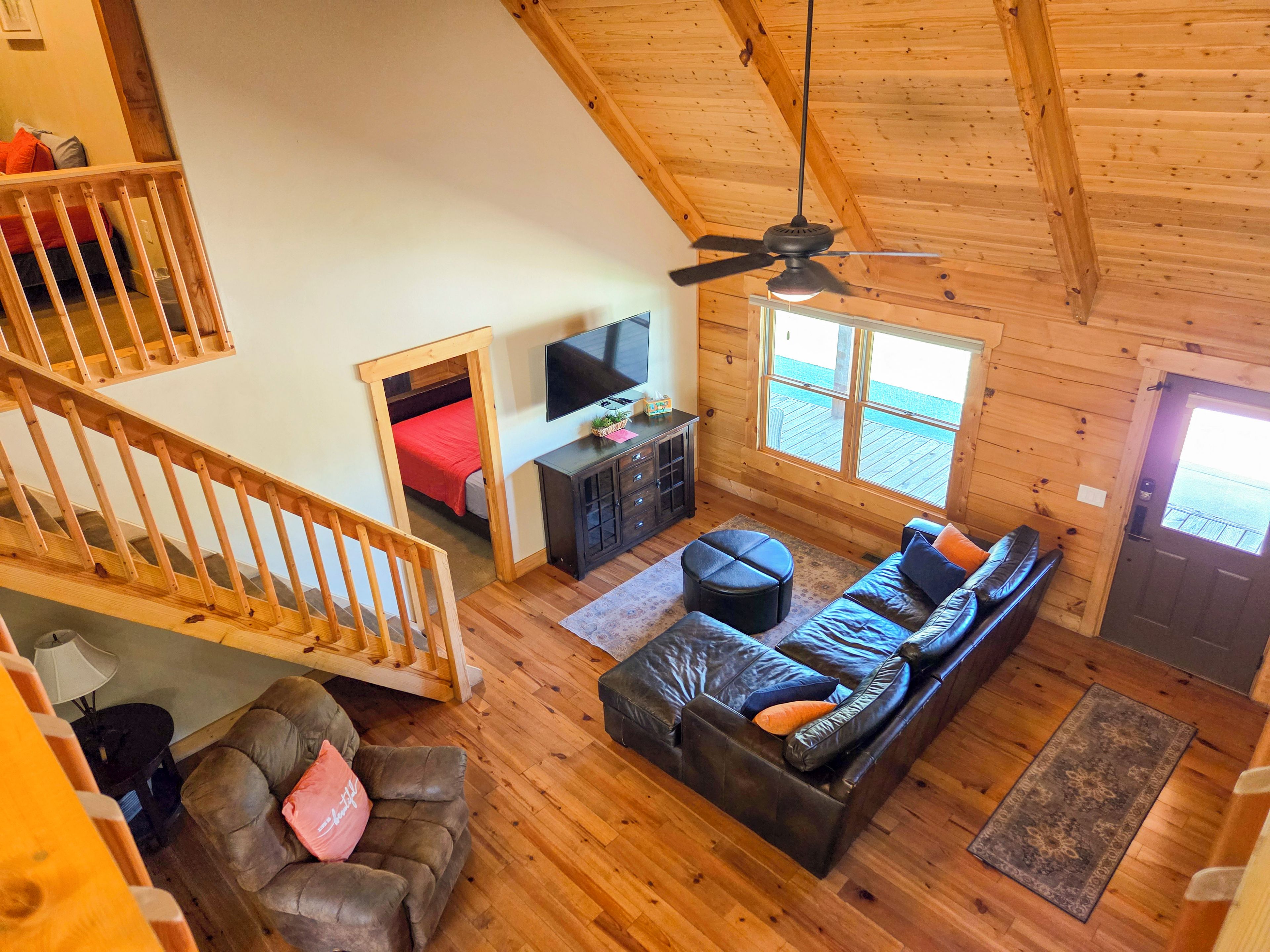 Een loft-achtige kamer met houten plafond, een trap, een zithoek, een televisie en een raam met uitzicht op een terras.