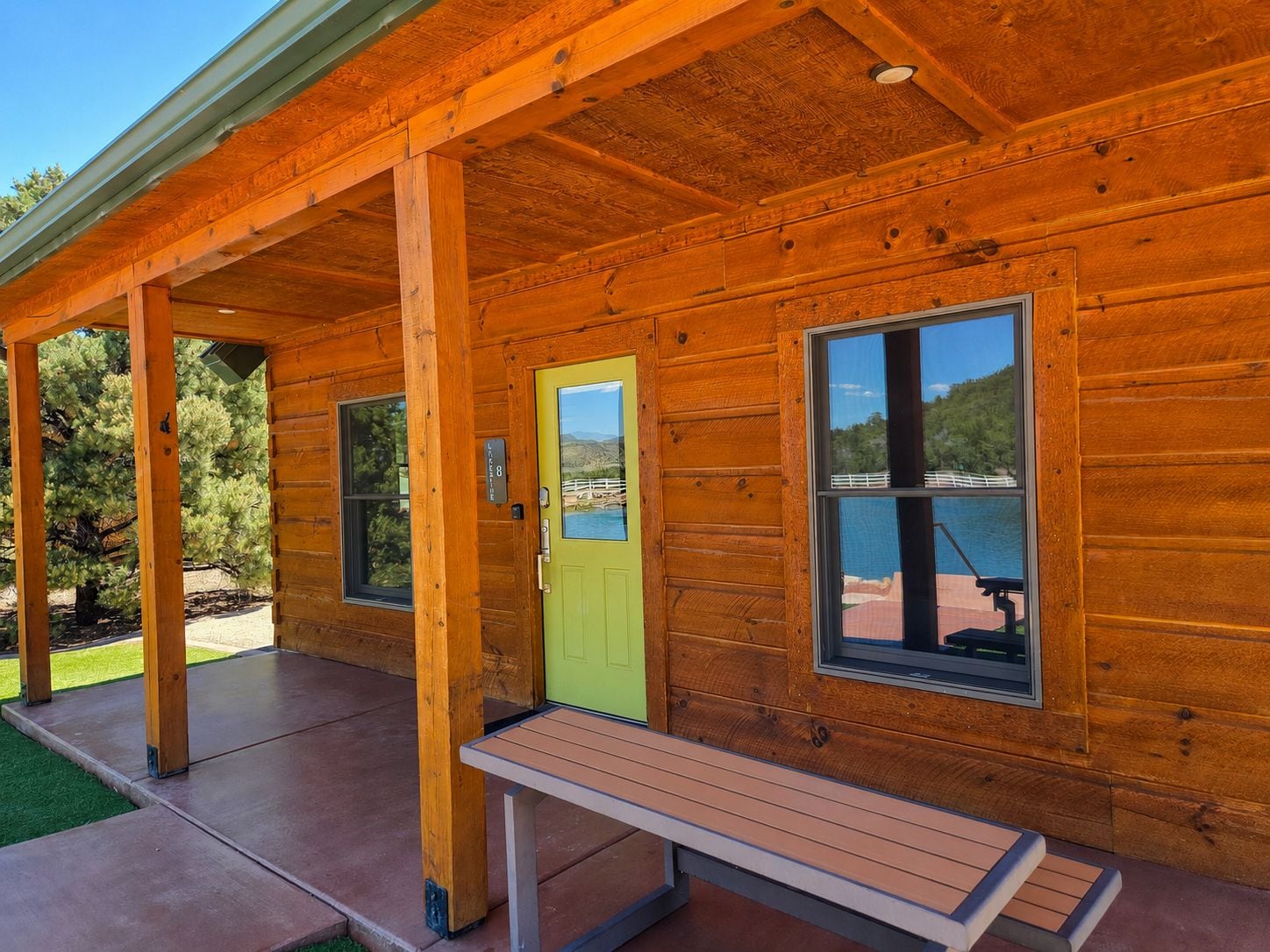 A wooden cabin with a covered porch, a green door, and a bench.