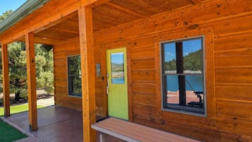 A wooden cabin with a covered porch, a green door, and a bench.