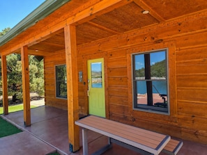 A wooden cabin with a covered porch, a green door, and a bench.