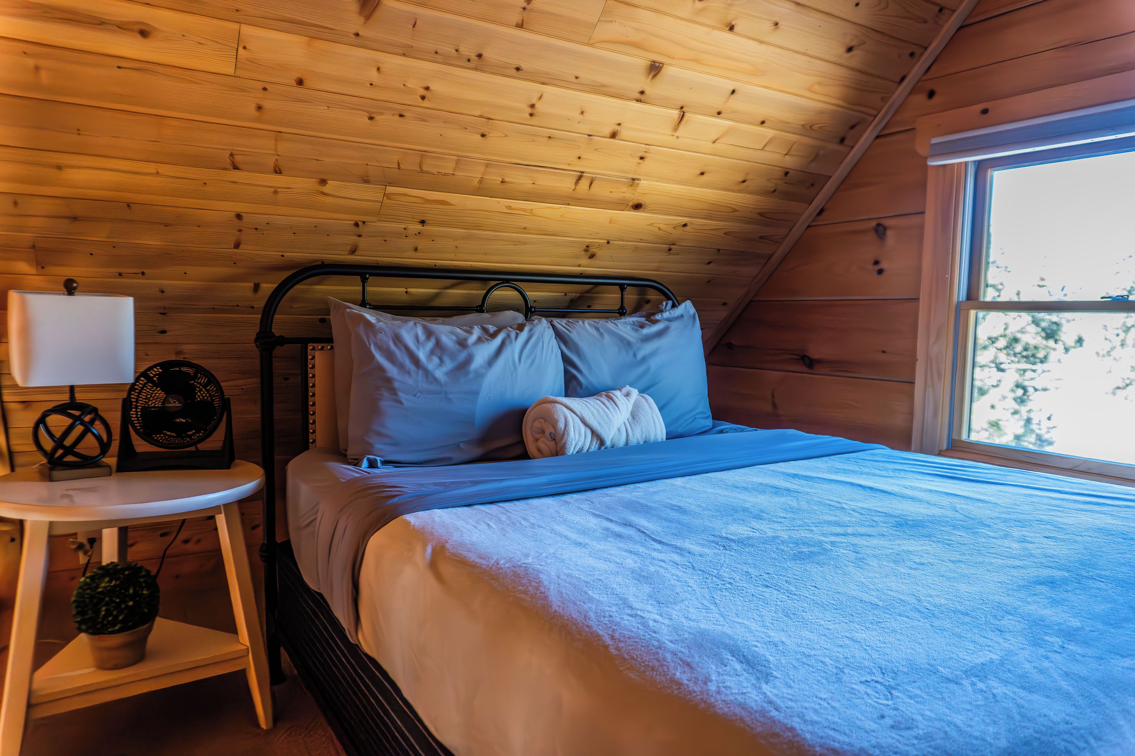 A bedroom with a bed, a bedside table, a lamp, and a window.