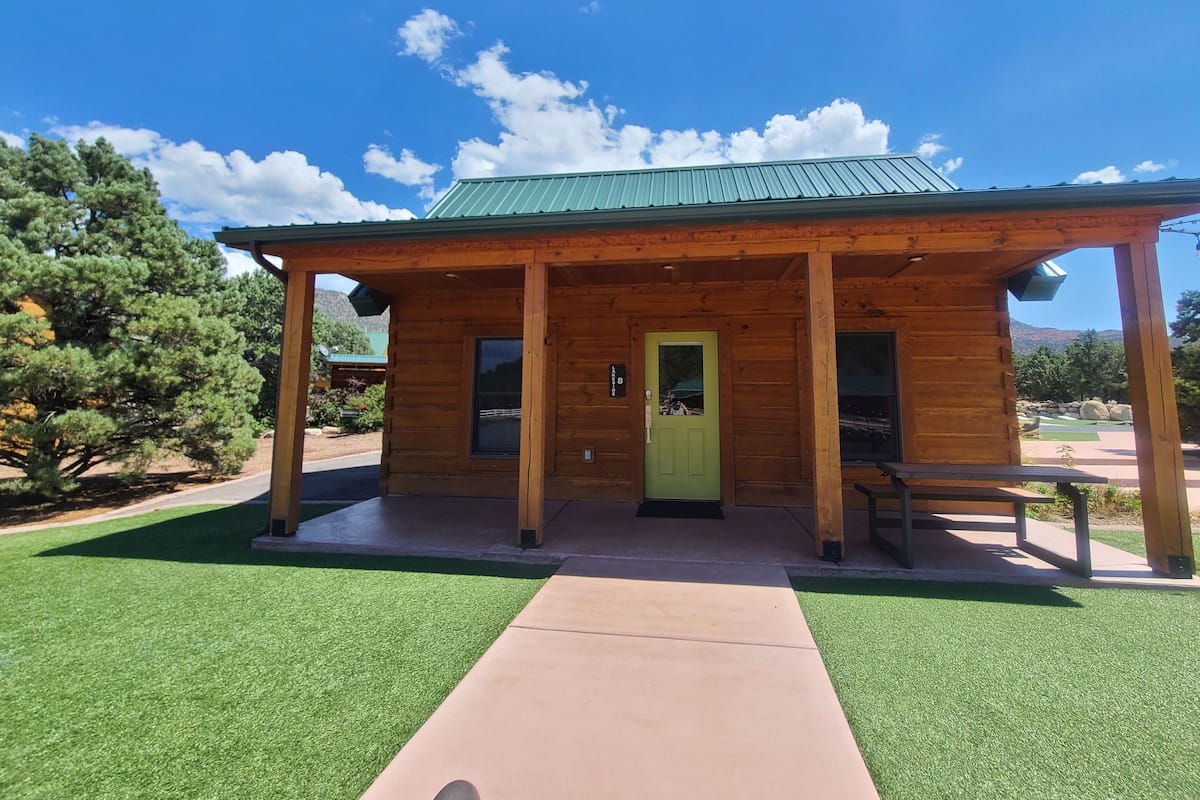 A wooden cabin with a green door, a covered porch, and a clear view of the surrounding landscape.