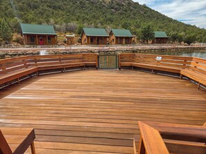 A wooden deck with benches, a stone wall, and cabins with green roofs. - Holmstead Ranch Resort (Veyo)