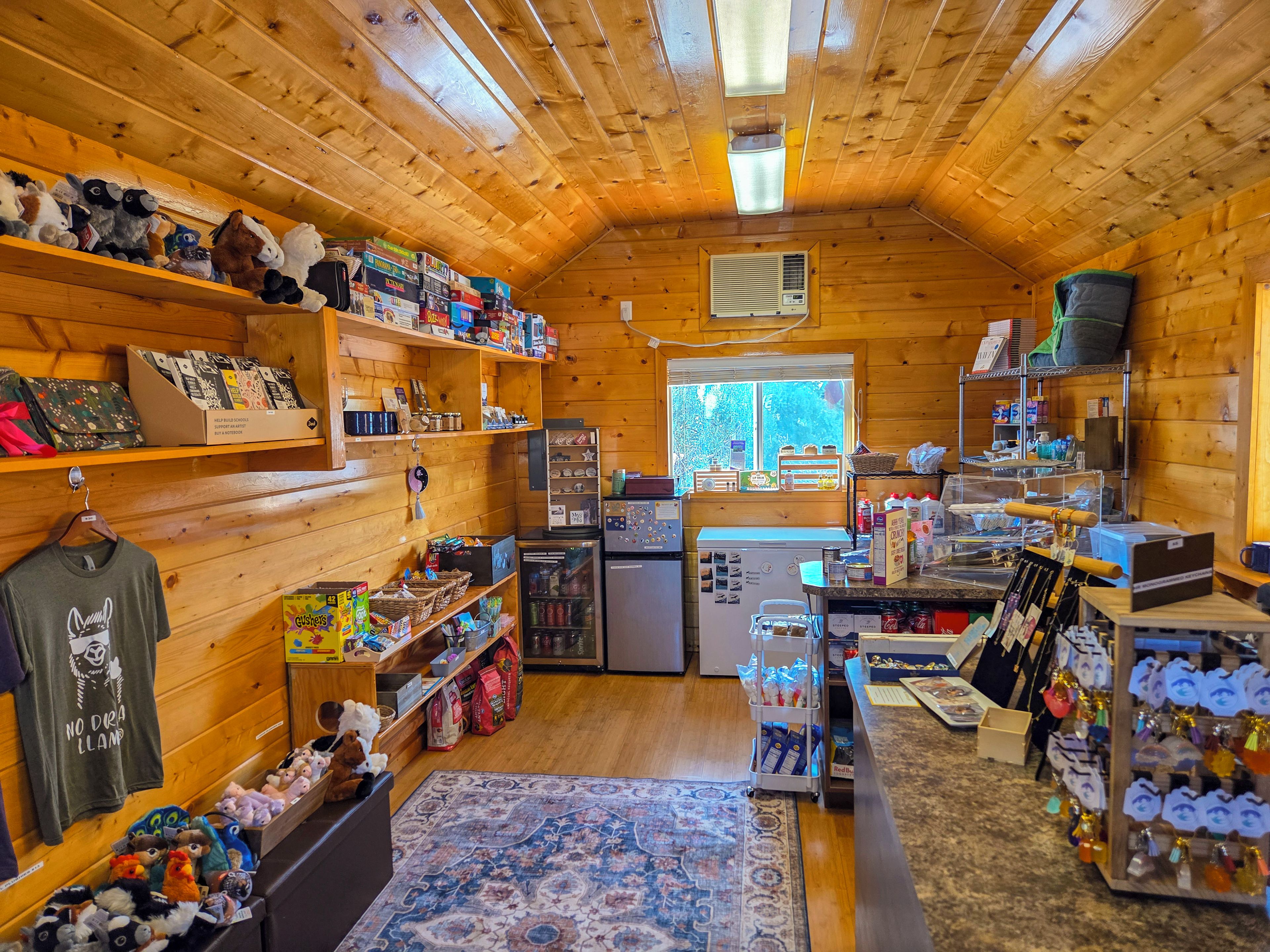 A cozy cabin interior with wooden walls, a kitchen area, and various items on shelves and counters.