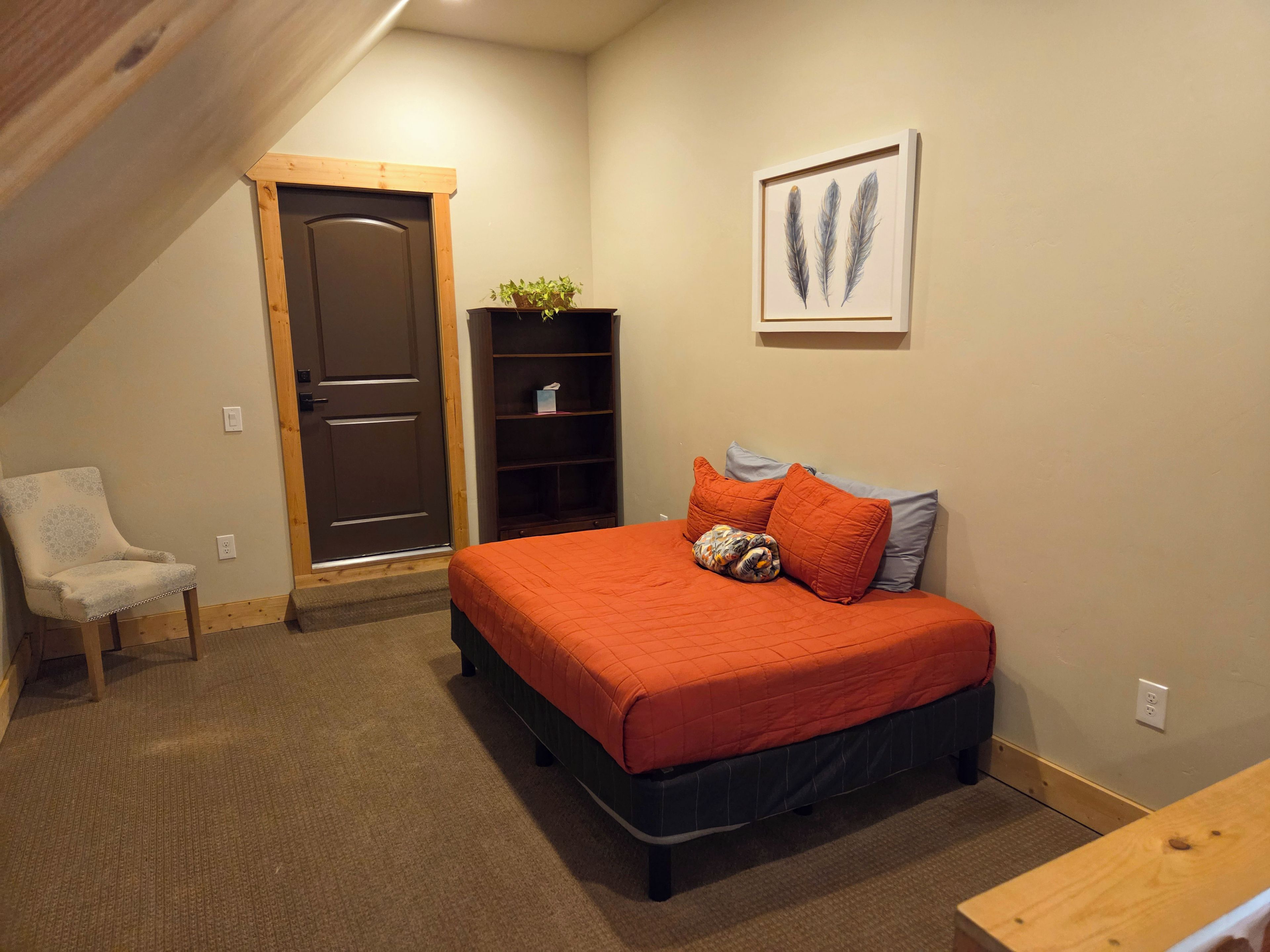 Een slaapkamer met een bed, een stoel, een boekenkast en een deur.