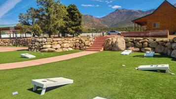 A lawn with several disc golf baskets, a stone wall, and a wooden building with a car parked nearby.